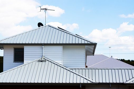 Modern corrugated iron roofs with tv antenna and satellite dish against sky with white clouds, full frame horizontal composition