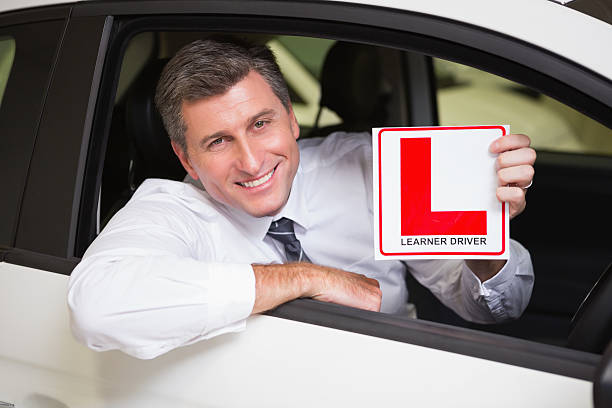 istock Man holding a learner driver sign sitting behind the wheel 468708794