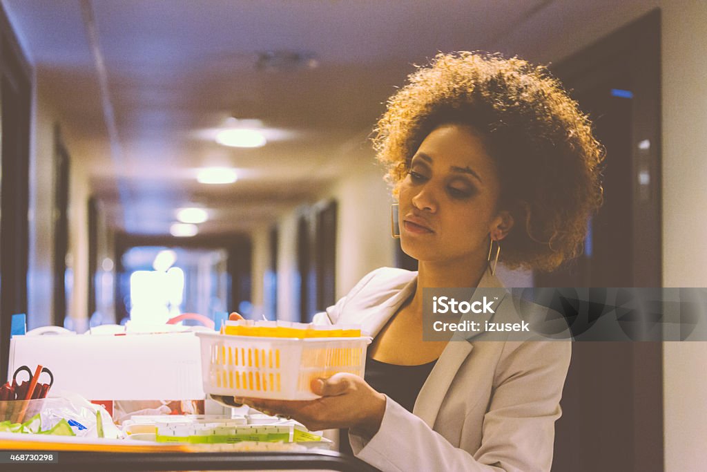 Room service female manager at work Afro amercian woman - room service female manager standing  in hotel corridor next to trolley with toiletries and chcecking products. Hotel Stock Photo