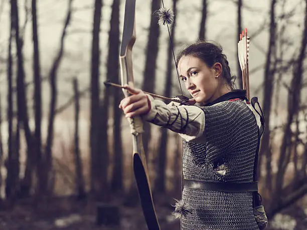 Medieval archer woman, she wearing a chainmail and use a bow and arrow, gloomy forest, cross-processed image.