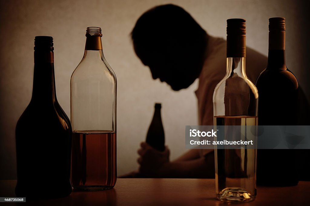 Alcohol bottles with the Silhouette of an alcoholic man silhouette of a person drinking behind bottles of alcohol with added filter                             Alcohol Abuse Stock Photo