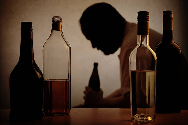 Alcohol bottles with the Silhouette of an alcoholic man silhouette of a person drinking behind bottles of alcohol with added filter                             alcohol abuse stock pictures, royalty-free photos & images