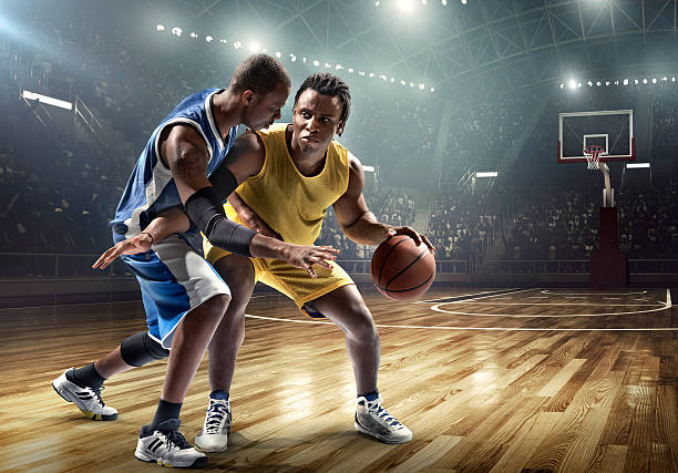 One on one basketball game in the spotlight Low angle view of a professional basketball game. A player is trying to block  the opposite team player with a ball. A game is in a indoor floodlit basketball arena. All players are wearing generic unbranded basketball uniform. offense sporting position photos stock pictures, royalty-free photos & images