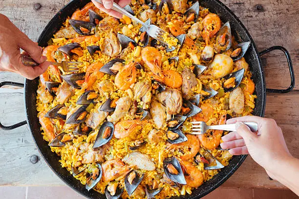 Mixed paella and hands with forks taking rice. Aerial view.