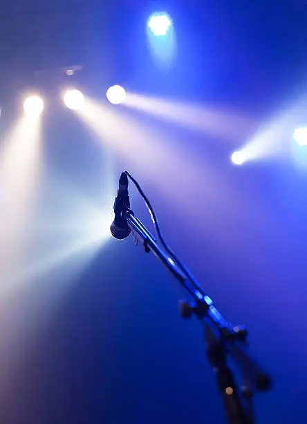 Photo of Microphone on a stand against a stage backdrop with lights