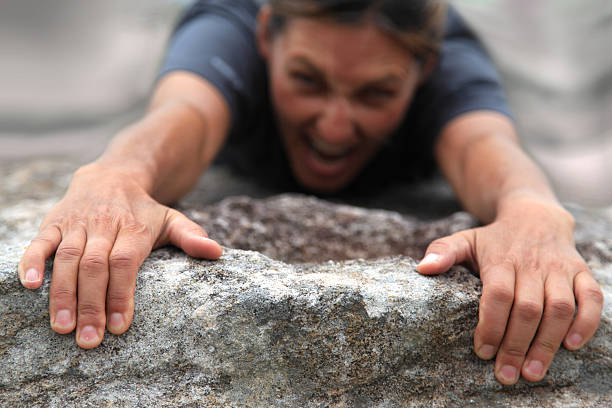 Determination Rock climber haning on to the edge of a cliff. Shere determination and endurance. gripping stock pictures, royalty-free photos & images