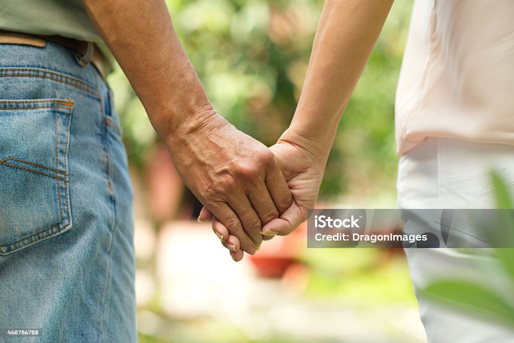 Holding hands Holding hands of mature couple walking outdoors Rear View Stock Photo