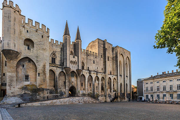 Avignon, France - June 10, 2014: Early morning in Place du Palais, where only few people are strolling. On this square overlooks the Palais des Papes, where Pope John XXII moved the papal seat in 1316 and where it remained for the eight popes that followed.
