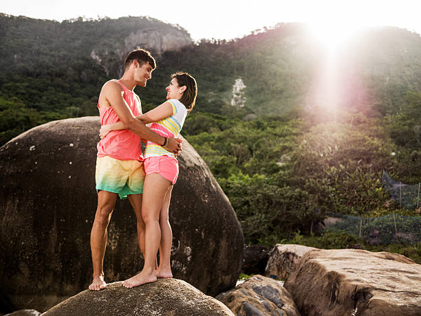 Happy Latin American couple standing embraced on the rock during summer day and communicating.