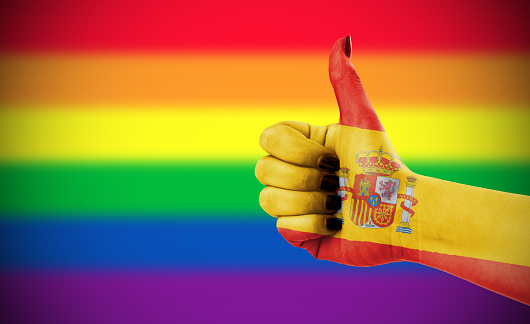 Concept photo - Positive attitude of Spain for LGBT community. Hand against rainbow flag. Focus set on hand.