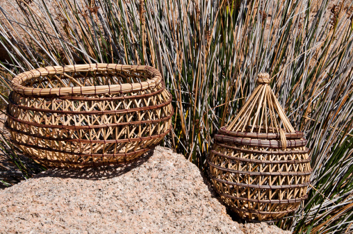 two traditional braided Corsican baskets placed on a pink granite rock with plant stems in the background