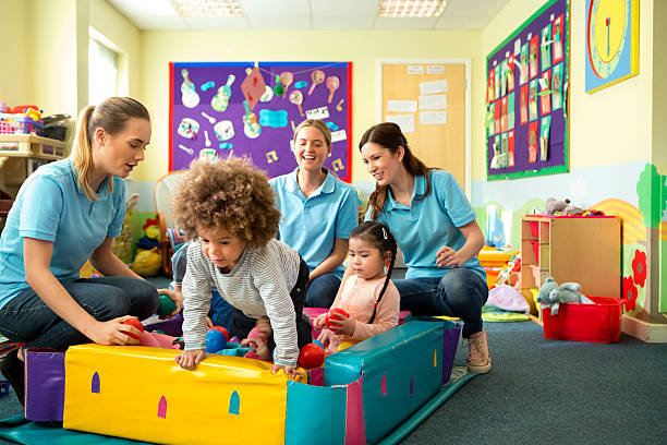 Ball Pool Fun A horizontal image of a group of children in a ball pool playing and laughing, behind them sit three nursery teachers in blue polo shirts supervising and smiling. The nursery is a colourful scene of toys and mess. two groups stock pictures, royalty-free photos & images