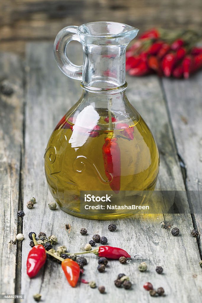 Olive oil with chili peppers Glass bottle of olive oil with red hot chili peppers over old wooden background. See series Backgrounds Stock Photo