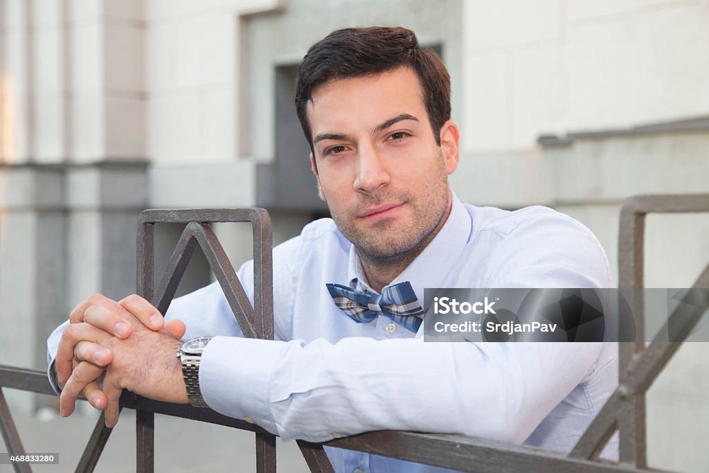 Handsome young gentleman Portrait of a handsome young man,leaning on the fence and looking at the camera. He is wearing an elegant blue shirt and a plaid bow tie. 2015 Stock Photo