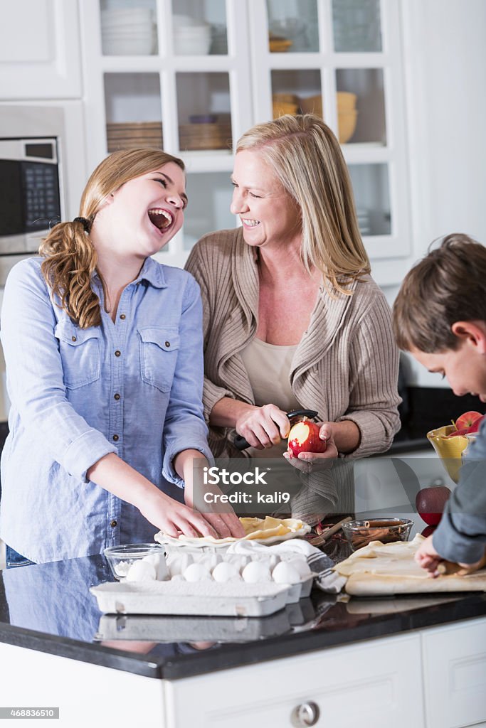 Teenagers in kitchen helping mom bake pie A teenage girl and her brother helping their mother in the kitchen, baking an apple pie.  The girl is laughing while she talks to her mom.  She is making the crust while mom peels and apple and her brother using the cutting board. 14-15 Years Stock Photo