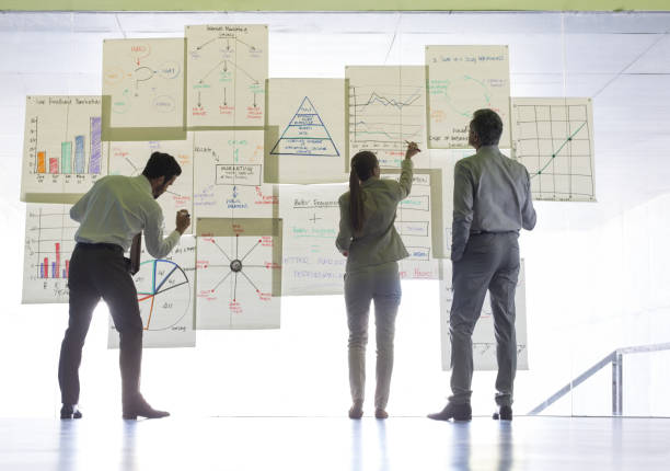 geschäftsleute arbeiten mit diagrammen und grafiken auf glaswand - hängen grafiken stock-fotos und bilder
