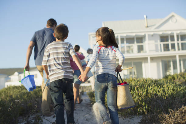 frère et soeur tenant les mains sur le chemin menant à la plage - maison de vacances photos et images de collection