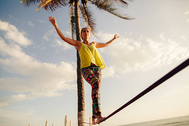 A teenage girl balancing on a rope beneath the sunny skies teenage girl  balancing on slackline with sky view on the beach highlining stock pictures, royalty-free photos & images