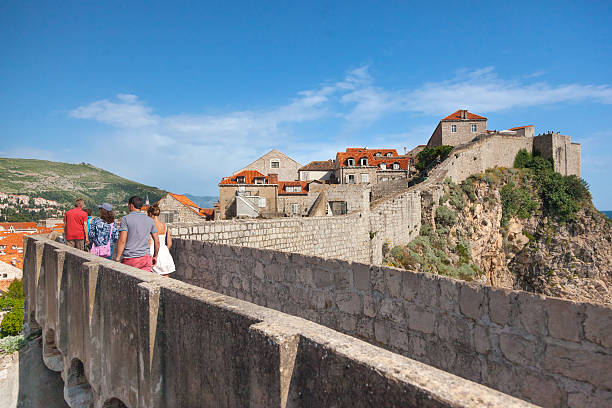 People walking on the city walls Dubrovnik, Croatia - May 26, 2014: People walking on the city walls with old houses in background. City wall is one of most popular tourist attraction in Dubrovnik. dubrovnik walls stock pictures, royalty-free photos & images