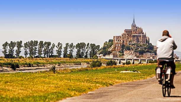 Mont Saint-Michel, Normandy, French Mont Saint-Michel, Francia. July 9, 2014. A tourist reaches Mont Saint Michel by bicycle along a scenic bike path along the Seine. tidal inlet stock pictures, royalty-free photos & images