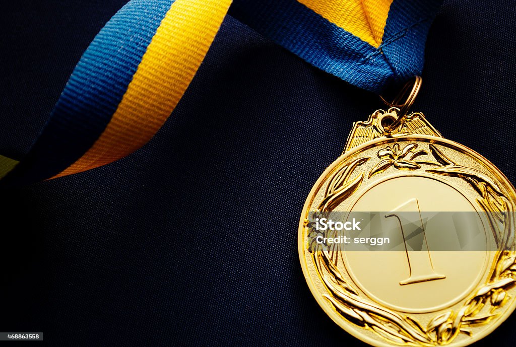 Gold medal on a dark blue background Gold medal in the foreground on yellow blue ribbon Medal Stock Photo