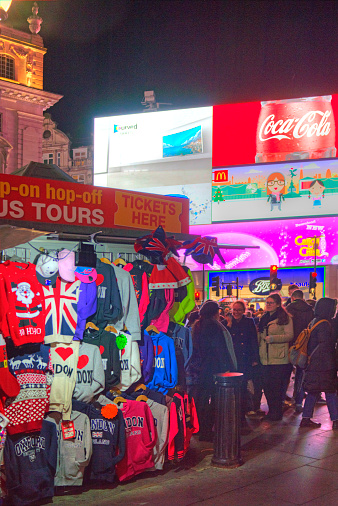 London, United Kingdom - December 7, 2014: Piccadilly Circus in London's West End.  This scene is taken at night with a high ISO and shows tourists and a gift stall in the foreground. This image was post processed in HDR software and Photoshop elements to enhance the atmosphere and reduce noise.