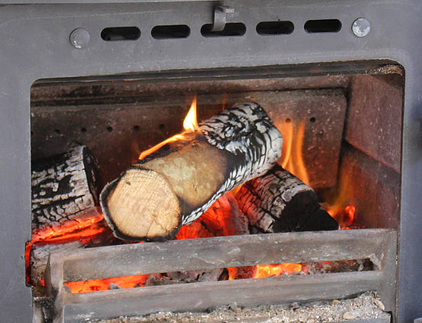 Photo showing the inside grate of a traditional cast iron woodburner, pictured with its door open to reveal the logs, flames and fire burning inside.  Metal wood burning stoves are often referred to as multi-fuel stoves, since they are able to burn either wood or alternatively, a smokeless fuel, such as coke, coal or charcoal options.