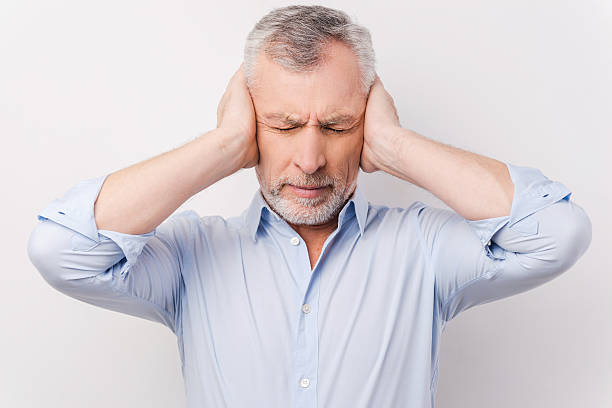 This is too loud for me! Frustrated senior man in shirt holding head in hands and keeping eyes closed while standing against grey background hands covering ears stock pictures, royalty-free photos & images