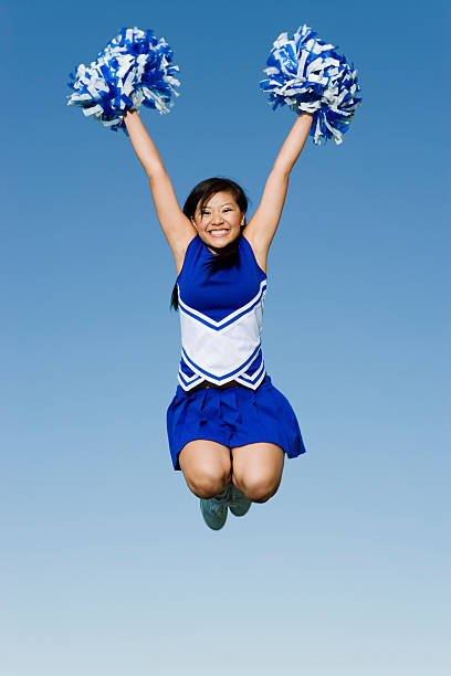 Cheerleader Performing Cheer in Mid-Air Full length of excited cheerleader with pompoms in midair against blue sky cheerleader photos stock pictures, royalty-free photos & images