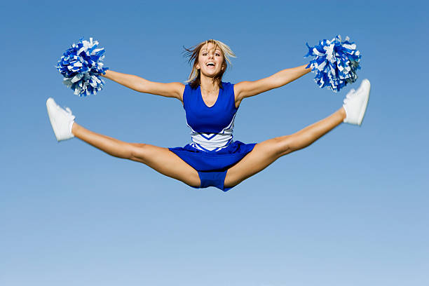 Cheerleader With Pompoms Doing Splits Against Sky Full length of excited cheerleader with pompoms doing splits against blue sky cheerleader photos stock pictures, royalty-free photos & images