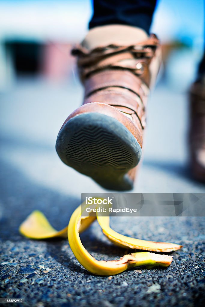 Slippery situation! Booted foot aproaching banana skin on street An unidentified  walker's foot in boots is about to step on a dropped banana peel - a possibly dangerous, painful and costly event! 2015 Stock Photo