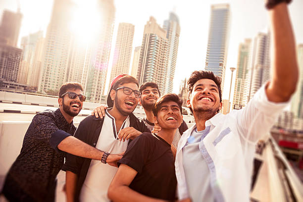Group of happy friend spending some time together taking selfies during their summer vacation in Dubai. They are in Dubai Marina district, sunlight on the background and having fun embracing and smiling on camera.