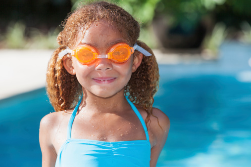 Little girl wearing goggles, standing next to swimming pool.  Mixed race African American / Caucasian, 5 years.