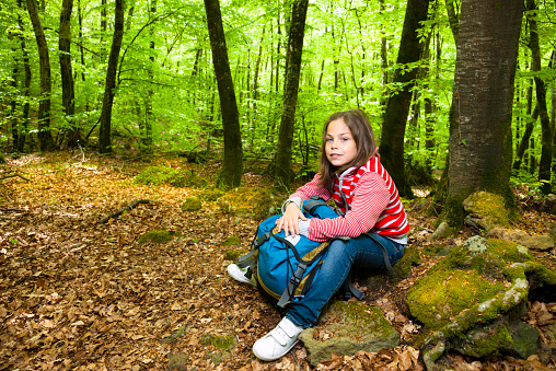 Ten years old girl sitting in a beech forest. Se has a backpack.