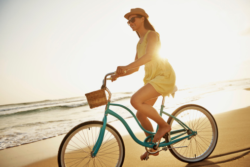 An attractive young woman cycling barefoot on the beach