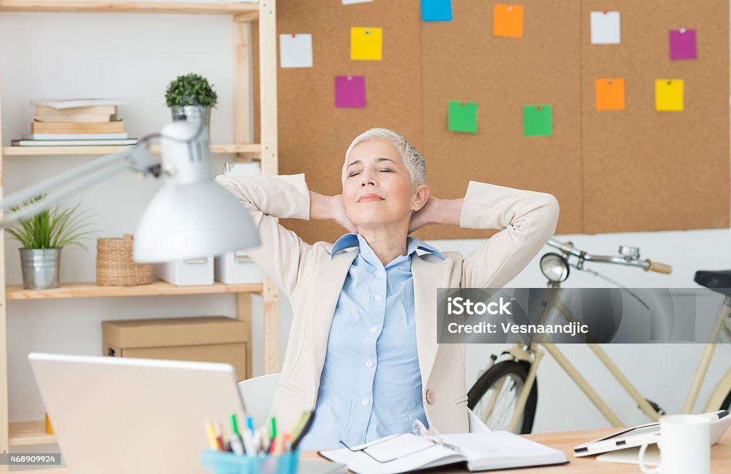 Beautiful cheerful mature woman at office relaxing Beautiful cheerful mature woman at office working on computer, pause for relaxing 2015 Stock Photo