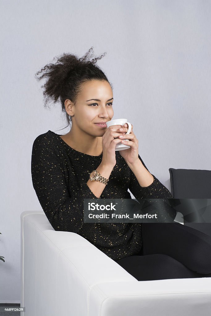Young woman drinks a cup of coffee Young, beautiful woman sits on the couch and drinks a cup of coffee in the freetime. Adult Stock Photo