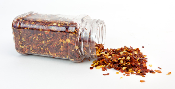 Crushed red pepper spilling from clear plastic bottle. Horizontal.