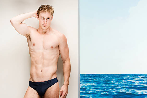 muscolare uomo appoggiato sulla parete di fronte alla spiaggia - men swimming trunks beach racing briefs foto e immagini stock