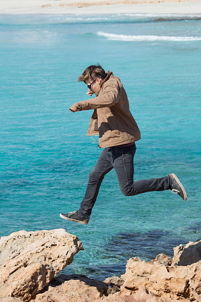 istock Young man bounds along coastline rocks 468922372