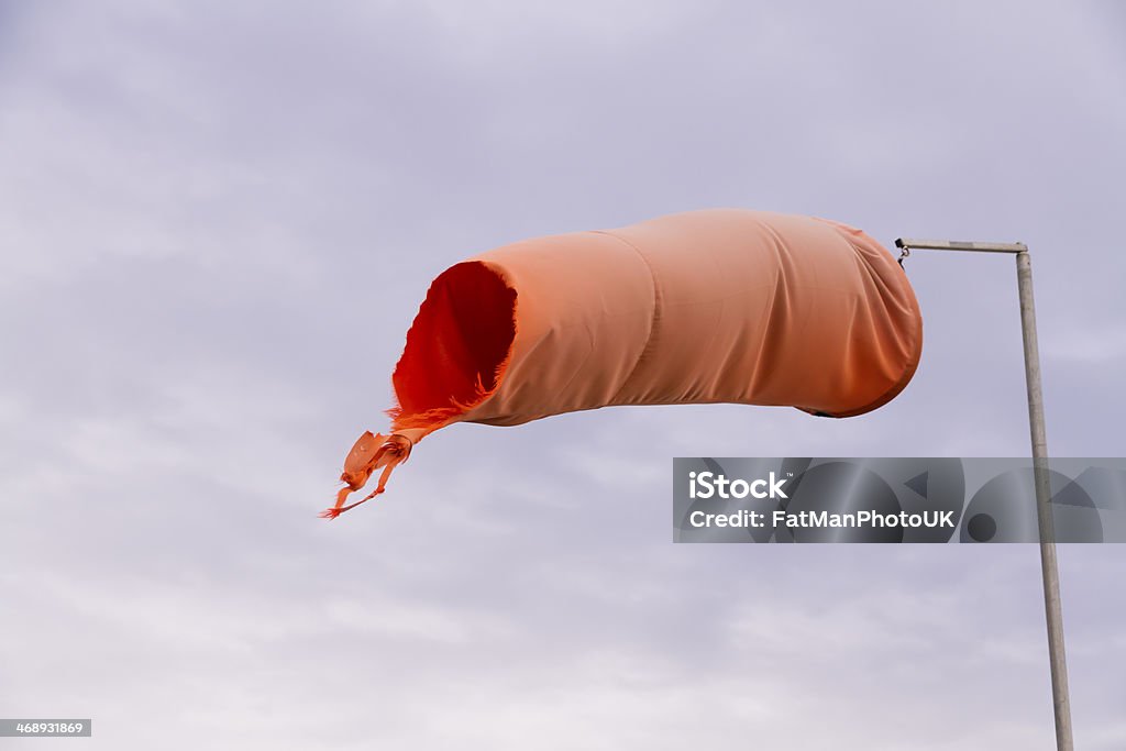 Red weathered windsock Wind sock (or conical textile tube) red and worn at one end against a grey sky. Airfield Stock Photo Red weathered windsock Wind sock (or conical textile tube) red and worn at one end against a grey sky. Airfield Stock Photo