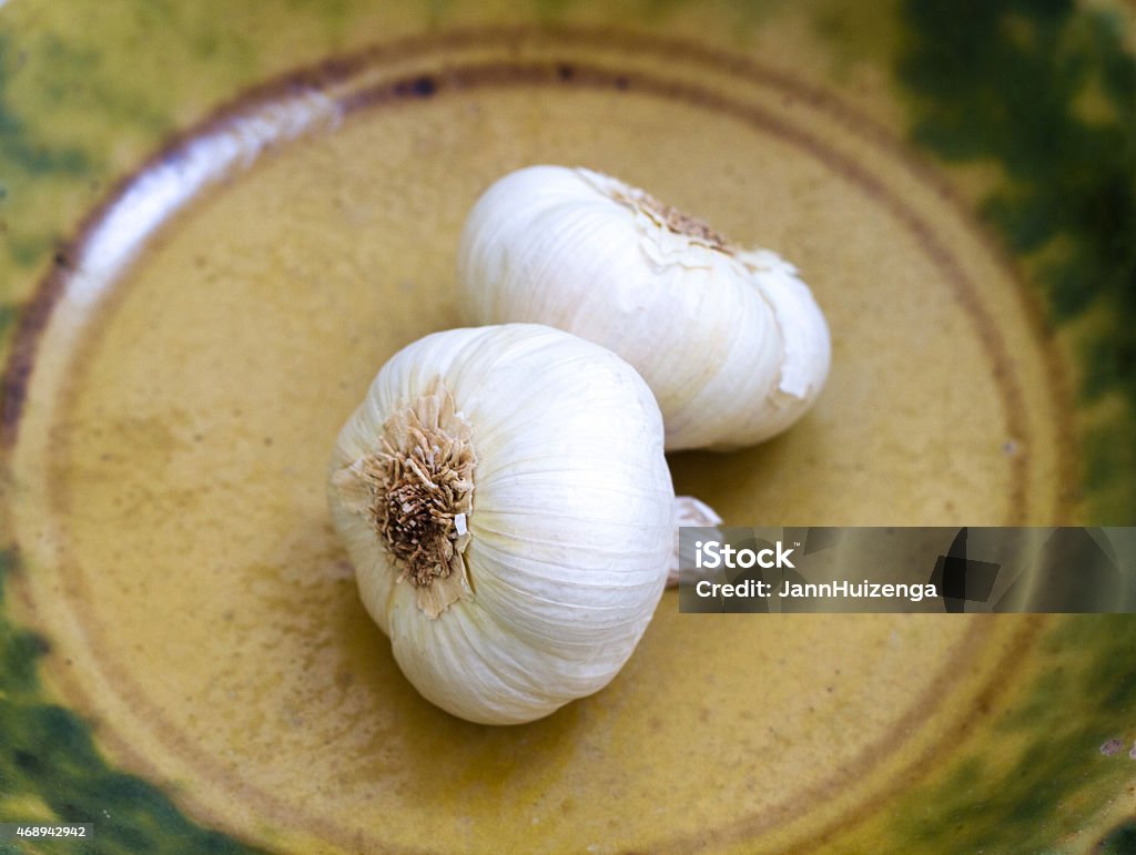 Pair of Garlic Bulbs in Antique Yellow-Green Ceramic Bowl Pair of garlic bulbs in an antique yellow-green ceramic bowl. 2015 Stock Photo