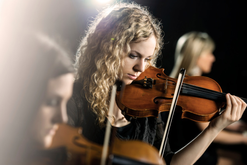 Three women playing musical instruments. Focus is on the middle, on young woman playing violin.