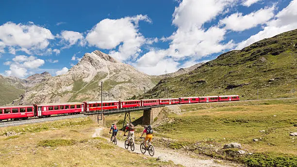 Three mountainbikers on their way down from the Bernina Pass are crossing the Bernina railway. It is a single track railway line forming part of the Rhaetian Railway. It links the spa resort of St. Moritz, in the Canton of Graubünden, Switzerland, with the town of Tirano, in the Province of Sondrio, Italy, via the Bernina Pass. Reaching a height of 2,253 metres (7,392 ft) above sea level, it is the highest railway crossing in Europe. It also ranks as the highest adhesion railway of the continent, and - with inclines of up to 7% - as one of the steepest adhesion railways in the world. The Bernina Railway is recorded in the list of UNESCO World Heritage Sites in 2008. The most famous trains operating on the Bernina Railway are known as the Bernina Express.