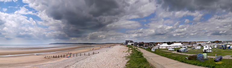 A panoramic picture taken near to Camber Sands in East Sussex. The image is made up of three photographs that have been stitched together in software. You can see Camber village, the sea defence wall and the sea. On the distant horizon, can be seen, the cliffs at Fairlight and Winchelsea bay.