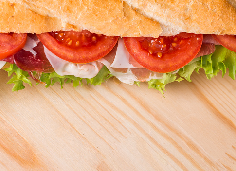 Ham and cheese salad submarine sandwich from fresh baguette on wooden background