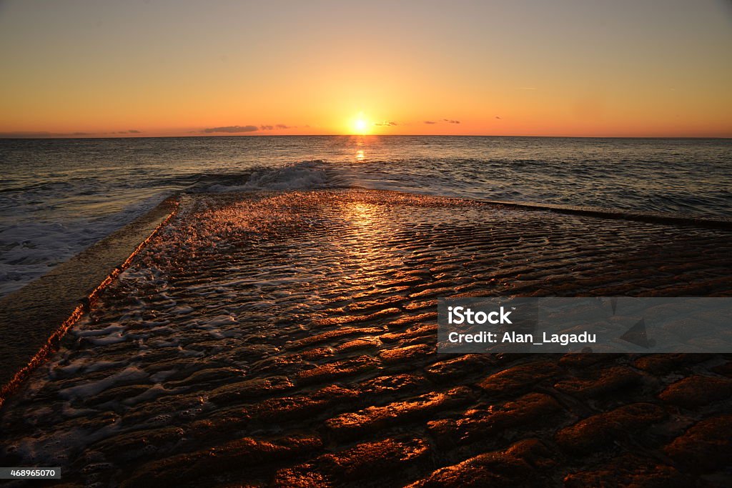 Jersey sunset, U.K. Wide angle coastal sunset with waves on the high tide, skipping over the cobbled slipway as it ebbs. 2015 Stock Photo