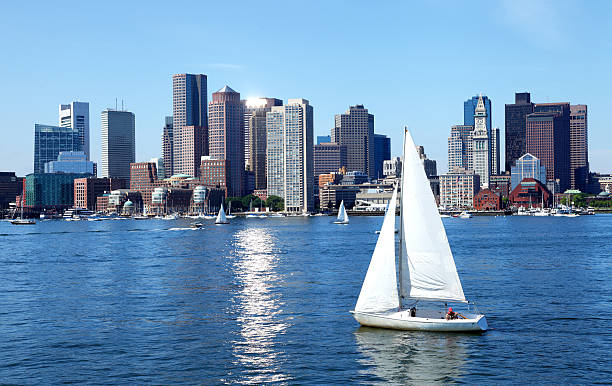 Sailboat along the Boston Skyline on the Boston Harbor waterfront. Photo of sailboats taken in the summer season from the East Boston eastie neighborhood. Boston cityscape is a mixture of old and new buildings. Boston is the capital and largest city in Masssachusetts. 
