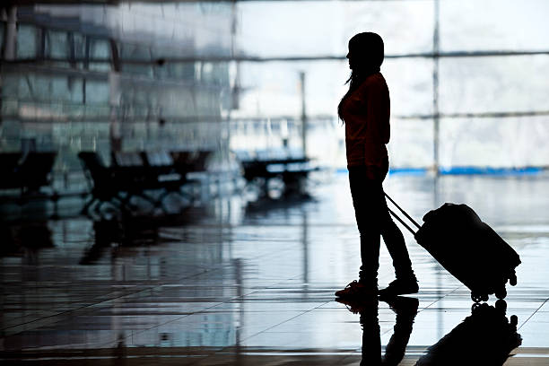 Silhouette of woman passenger walking through airport terminal with luggage