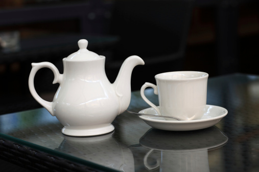 Teapot and teacup are on a glass table in a cafe